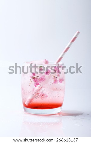 Ice cubes with pink flowers in glass  with paper straw on white background
