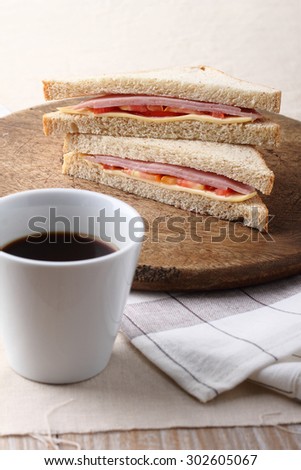 fresh sandwich with ham, cheese and tomato on wooden board\
with coffee for breakfast