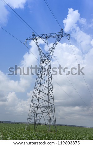 Electricity pylon crossing along a green field.