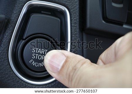 Close up shot of finger pressing the start/stop engine button on a car