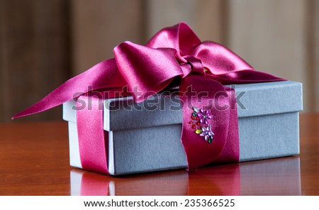 Holiday Gift Packed into Grey Box with Purple Ribbon on Glossy Wooden Table
