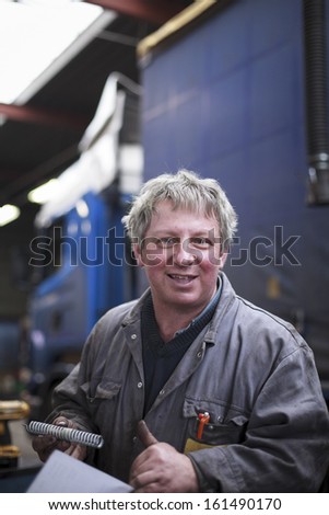 Gray haired mechanic smiling in a garage working on trucks