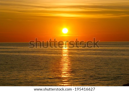 Beautiful golden orange sunset over the ocean. The sun sets turning the sky yellow, orange & red tones & reflects in the ocean.