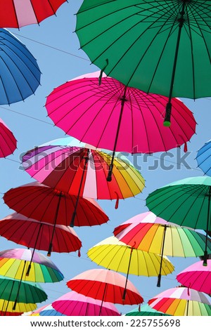 Collection of multi colored umbrellas hanging up in an open position over a street offering shade & protection from the elements.