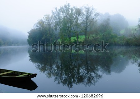 Foggy landscape with lake, Boat and tree reflection in a lake on a foggy early morning day,