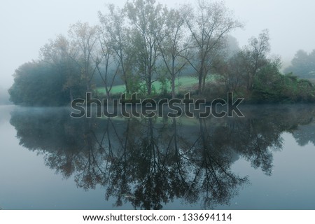 Misty morning lake with tree reflection in water. Foggy landscape with lake in Passau Germany.A town in Lower Bavaria Dreiflüssestadt or  City of Three Rivers - Danube