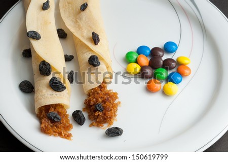 Rolled Pancakes with grated coconut filling, decorated with colorful sweet gems and dried grapes