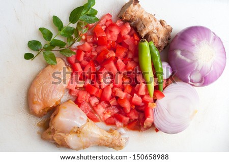 Raw chicken on cutting board with tomatoes onions and curry leaves. vegetables and herbs
