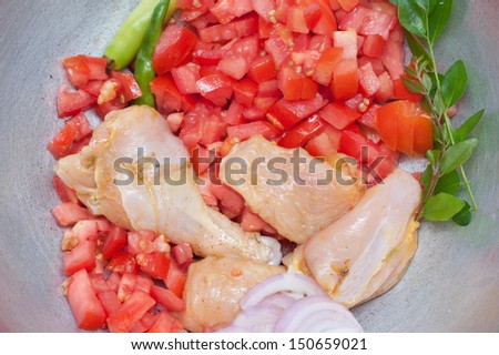 Raw chicken on cutting board with tomatoes onions and curry leaves. vegetables and herbs