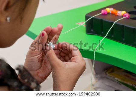 little girl making a necklace from wooden beads and a string. kids doing activity in play school  or  kindergarten