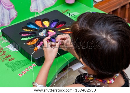 little girl making a necklace from wooden beads and a string.