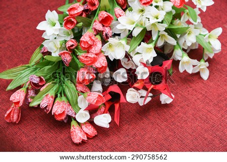 Colorful red tulips and white artificial flowers with green leaves on red jute background. used for interior decoration. artificial flower made with paper,thermocol and bamboo leaves for flower vase