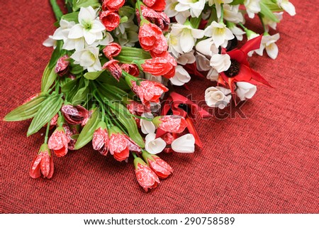 Colorful red and white artificial flowers with green leaves on red jute background.Colorful decoration artificial flower (vintage) can be put in a flower vase.used for interior decoration.