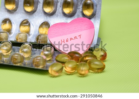 Cod liver fish oil omega 3 gel capsules isolated on green background. heart shaped paper copy space for text.