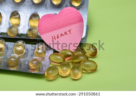 Cod liver fish oil omega 3 gel capsules isolated on green background.  heart shaped paper copy space for text. metal foil blister strip packaging.nutritional supplement contains Vitamin A , VitamineD