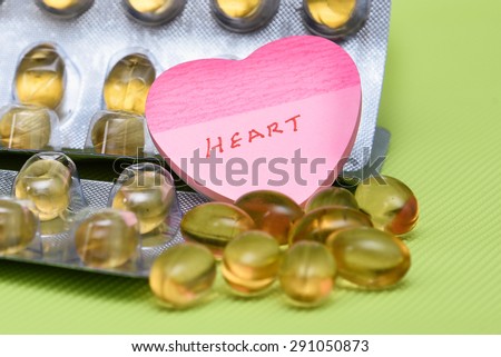 Cod liver fish oil omega 3 gel capsules isolated on green background. heart shaped paper copy space for text.