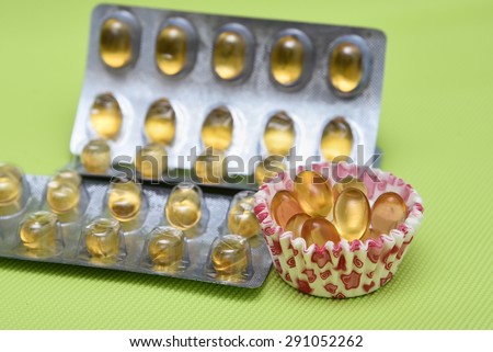 Cod liver fish oil omega 3 gel capsules isolated on green background. Golden yellow vitamin capsules in metal foil blister strip packaging. A nutritional supplement contains vitamin A and vitamin D.