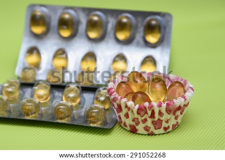 Cod liver fish oil omega 3 gel capsules isolated on green background. Golden yellow vitamin capsules in metal foil blister strip packaging. A nutritional supplement contains vitamin A and vitamin D,
