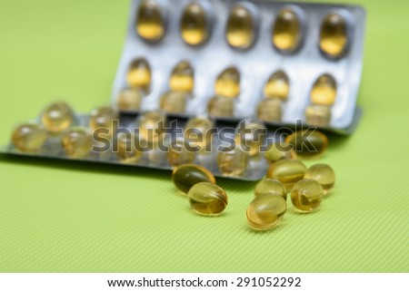 Cod liver fish oil omega 3 gel capsules isolated on green background. Yellow vitamin capsules in metal foil blister strip packaging