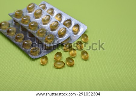 Cod liver fish oil omega 3 gel capsules isolated on green background.  Golden yellow vitamin capsules in metal foil blister strip packaging. A nutritional supplement contains vitamin A and vitamin D.