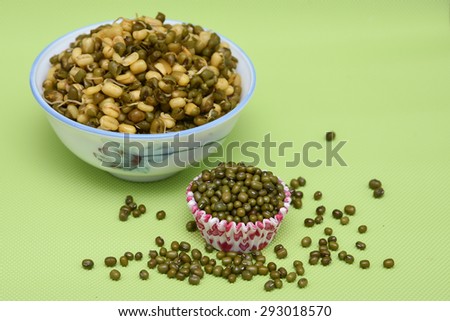 pile of seeds of green gram in a paper cup and scattered on green background