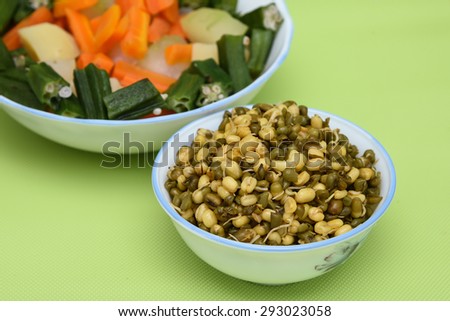 fresh vegetables carrot ladies finger potatoes cut up slices in bowls and sprouted seeds of green gram isolated on green