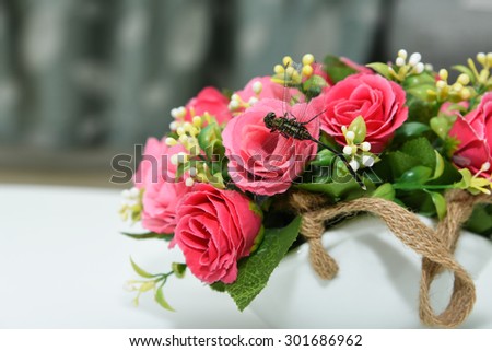 Dragon fly sitting on flower vase with beautiful red flowers. artificial flowers.