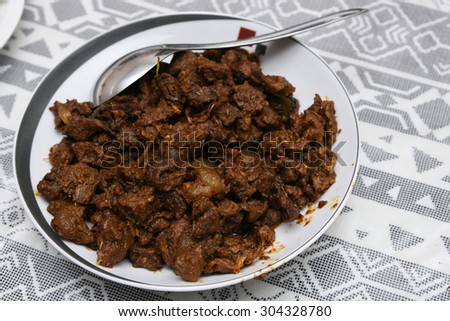 delicious spicy Beef fry in a white plate with spoon on a white textile background. It goes well with ghee rice, appam, parotta, puttu, bread and chappathi, Kerala style cuisine ,beef roast.India