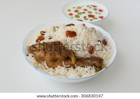 Chicken Biryani  or fried rice with fired chicken leg in white bowl on a white background .closeup view of delicious Indian chicken biriyani with colorful garnish, served with raita or curd.