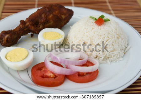 Cooked white rice with roasted chicken drumstick,egg,onion rings and tomato served on a white plate on bamboo mat  background.sticky rice, basmati ,jasmine rice garnished with tomato flower and herbs