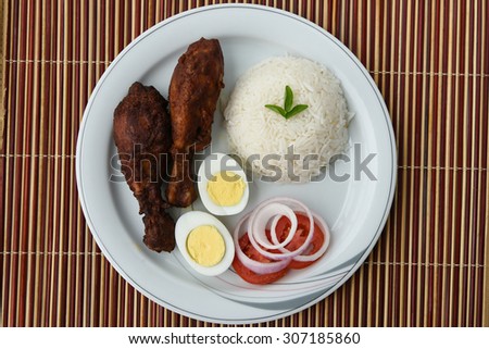 Cooked white rice with grilled chicken drumsticks,egg,onion rings and tomato slices on a white plate on bamboo mat  background.sticky rice, basmati ,jasmine rice garnished with tomato flower and herbs