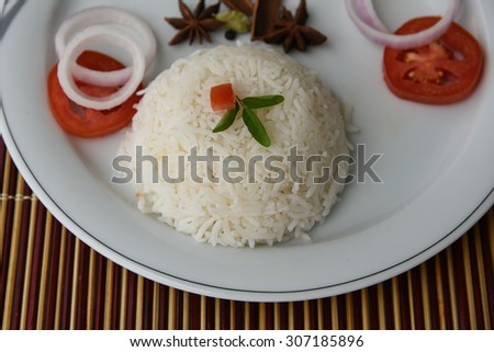 Cooked white rice with spices star anise,cloves,onion rings and tomatoes served on a white plate on a bamboo mat background .sticky rice, basmati or jasmine rice garnished with tomato flower and herbs