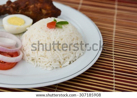 Cooked white rice with grilled chicken drumsticks,egg,onion rings and tomato served on a white plate on bamboo mat  background.sticky rice, basmati ,jasmine rice garnished with tomato flower and herbs