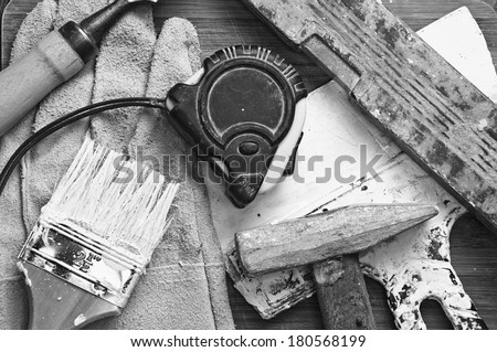 paint brush, level, hammer, putty knife stained with paint on wooden background