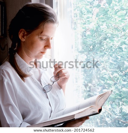 young girl reading a book next to the window