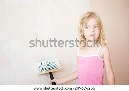 Little girl standing with a paint brush. Apartment repair. Wallpapering. Stock Photo