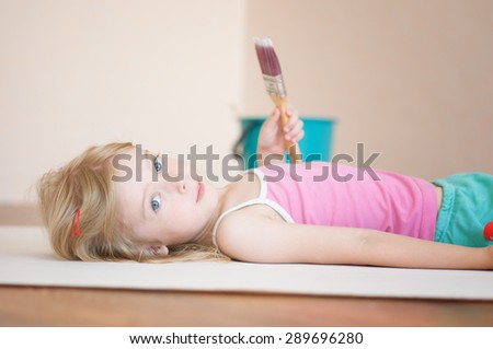 Little girl lies with a paint brush. Apartment repair. Wallpapering. Stock Photo