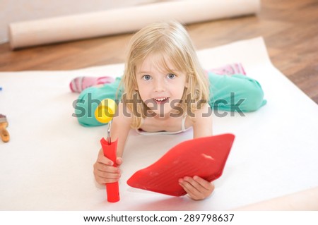 Little girl lies with a paint roller. Apartment repair. Wallpapering. Stock Photo