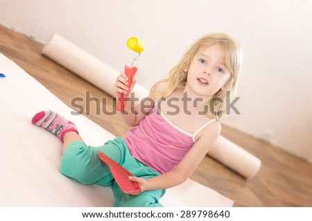 Little girl sitting with a paint roller. Apartment repair. Wallpapering. Stock Photo