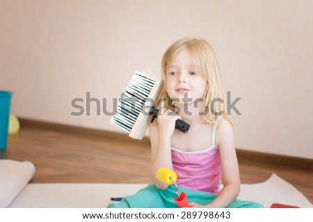 Little girl sitting with a paint brush. Apartment repair. Wallpapering. Stock Photo