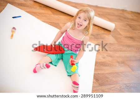 Little girl sitting with tools in his hands. Apartment repair. Wallpapering. Stock Photo