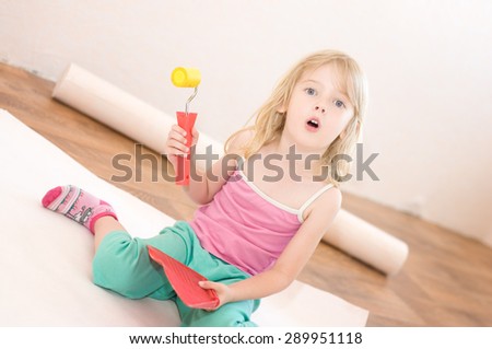 Little girl sitting with a paint brush and roller. Apartment repair. Wallpapering. Stock Photo