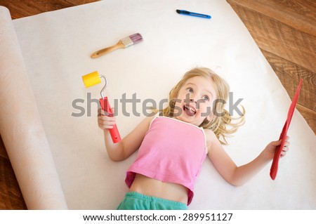 Little girl lies with a paint roller. Apartment repair. Wallpapering. Stock Photo