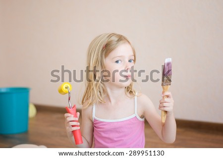Little girl sitting with a paint brush and roller. Apartment repair. Wallpapering. Stock Photo