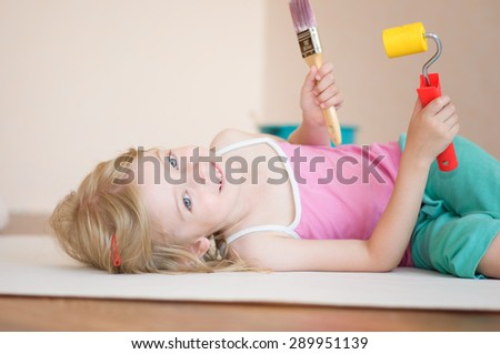 Little girl lies with a paint brush and paint roller. Apartment repair. Wallpapering. Stock Photo