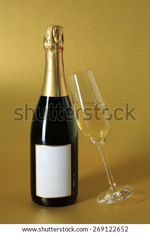 sparkling glass of champagne and bottle with blank label on golden background for jubilees