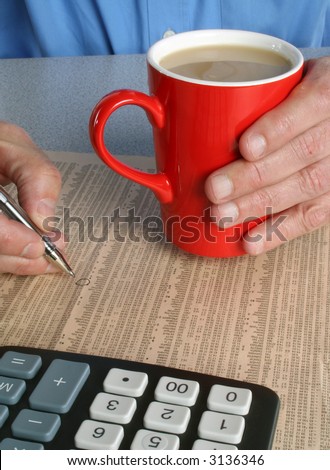 Man holding cup of coffee whilst selecting shares from newspaper.