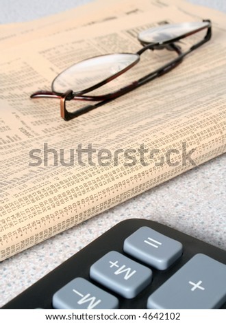 Spectacles rest on financial news paper. Focused on newspaper numbers.