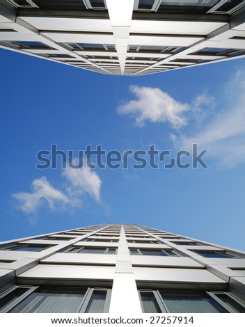 Tall office block against cloudy blue sky. Building mirrored for effect.