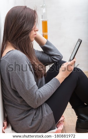 Profile of girl, seated on the floor, while reading an e-book.The text on the ebook reader is an \